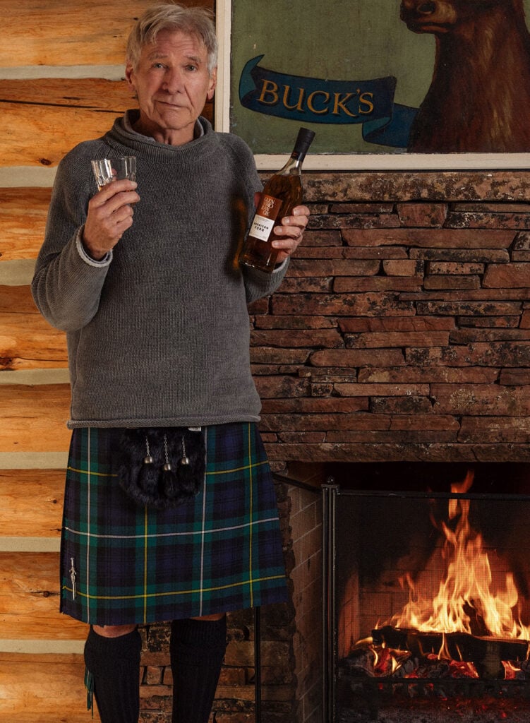 Harrison Ford with his own Glenmorangie whisky in front of a fire in a kilt